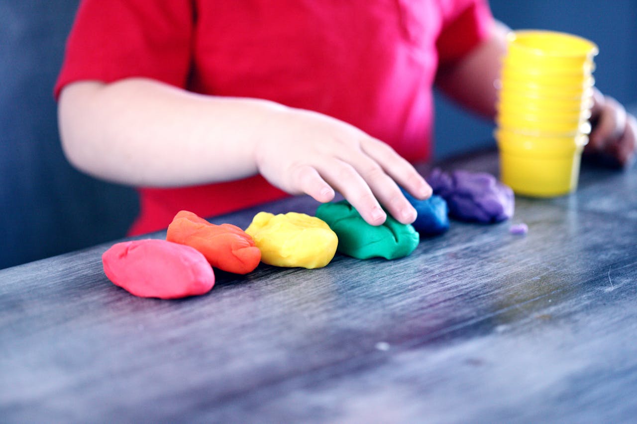services-bg A young child with rainbow-colored modeling clay and stacking cups on a table indoors.