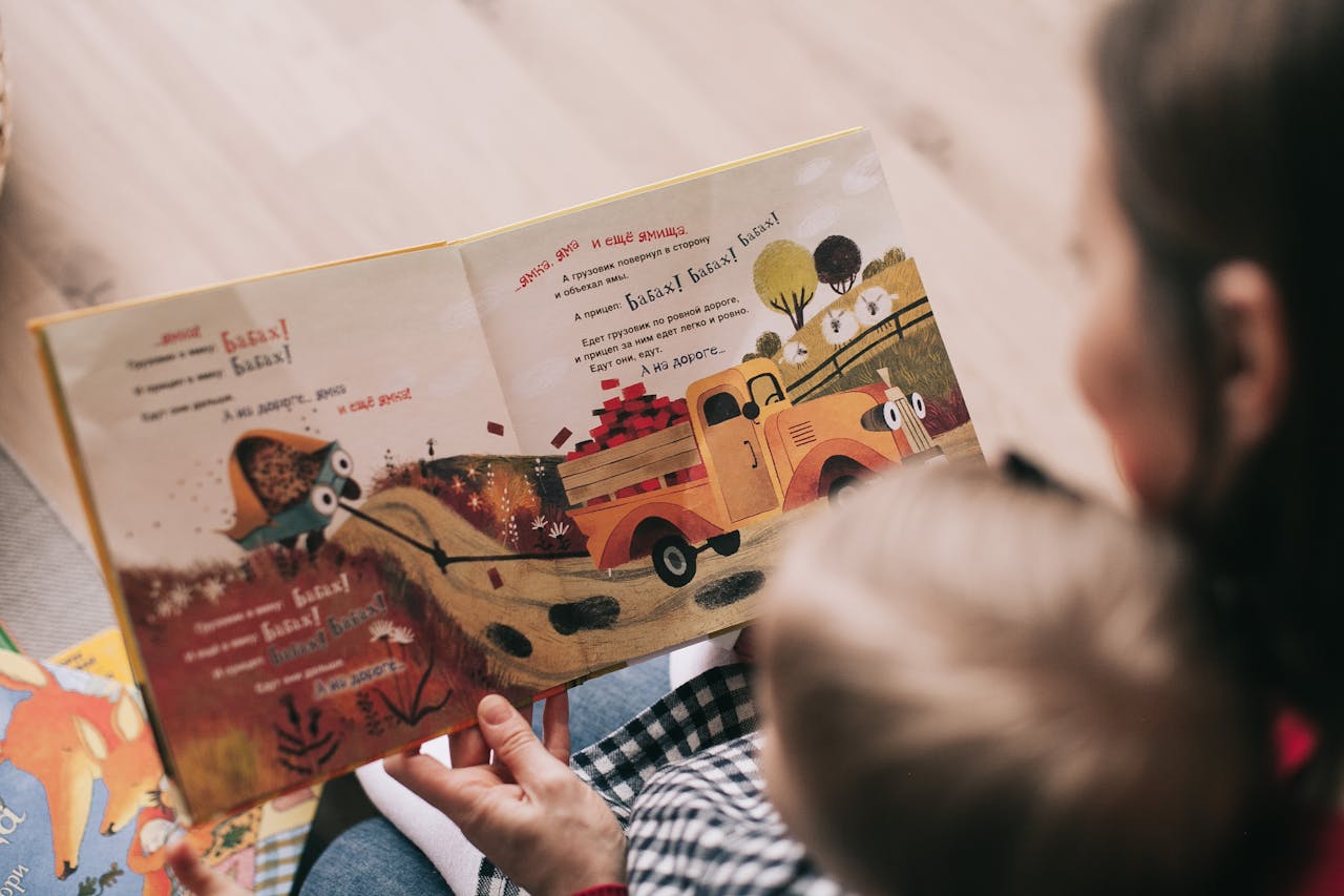 services-01 A mother and toddler sharing a story from an illustrated children's book indoors.